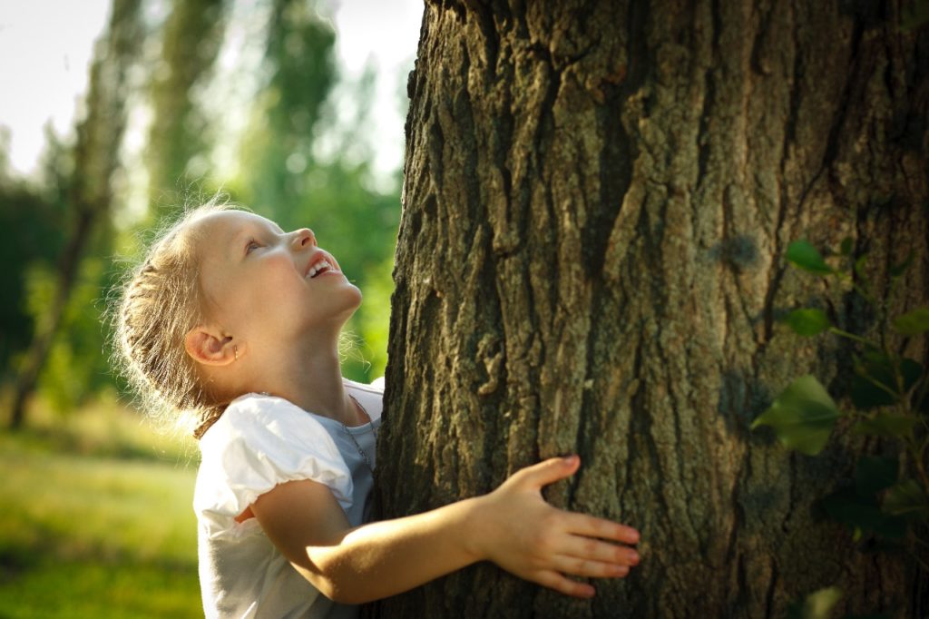 Menina abraça uma árvore. O futuro precisa ser sustentável.